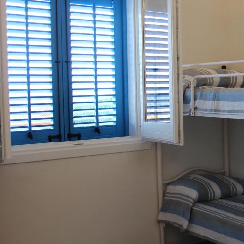 a bedroom with a window with blue shutters and a shelf at The twins Rooms in Marettimo 2 in Marettimo