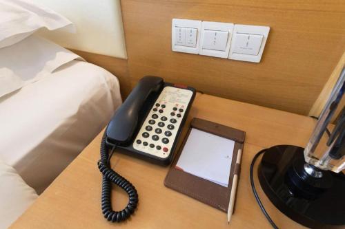 a telephone and a tablet on a table next to a bed at The Prosperous City Hotel Weifang in Weifang