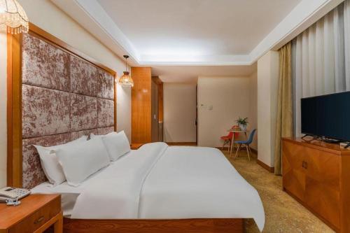 a bedroom with a large white bed and a flat screen tv at Lijiang Waika Hotel in Lijiang