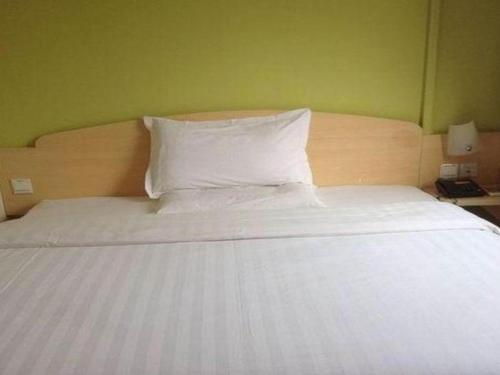 a bed with a white pillow and a green wall at 7 Days Inn Nanjing Gaochun Metro Station in Gaochun