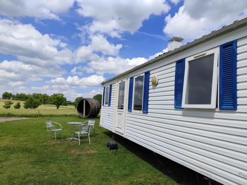 un remolque blanco con sillas y una mesa en un campo en La Billardière Camping à la Ferme, en Le Ménil-Ciboult