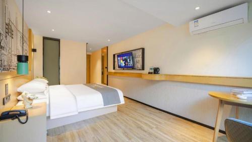 a bedroom with a bed and a table and a tv at City Comfort Inn Kunming High Speed Railway South Station Yongxin Harvard in Kunming