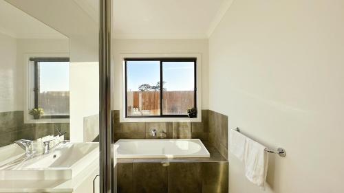 a bathroom with a tub and a sink and a window at Orchard Green Home by GoodLive in Melton South