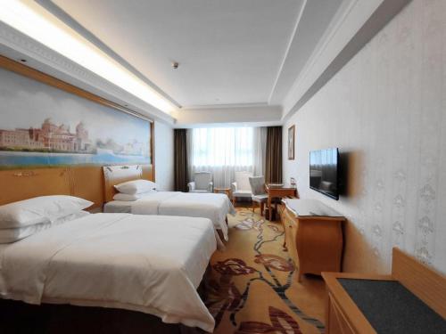 a hotel room with three beds and a television at Vienna Hotel Shenzhen Longhua Good Day in Tiantangwei