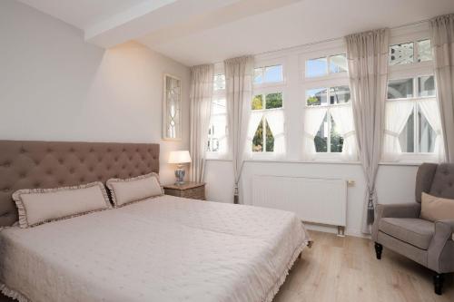 ein Schlafzimmer mit einem Bett und einem Stuhl und Fenstern in der Unterkunft Villa Eden Binz Typ 3 / Apartment 12 in Binz