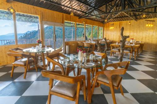 a restaurant with tables and chairs and windows at Ila by Aaryam, Kanatal in Chamba