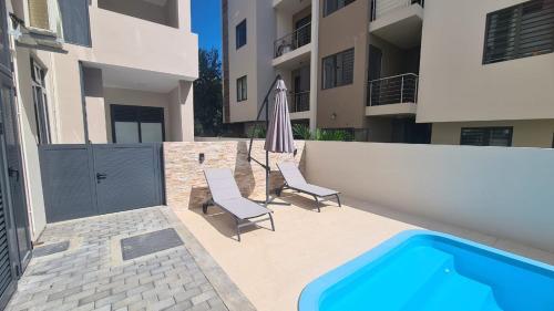 a swimming pool with two chairs and an umbrella next to a building at Cozy 2BR Retreat Flic en Flac in Flic-en-Flac