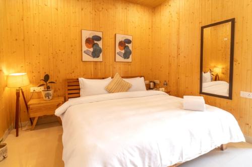 a bedroom with a large white bed and a mirror at Ila by Aaryam, Kanatal in Chamba