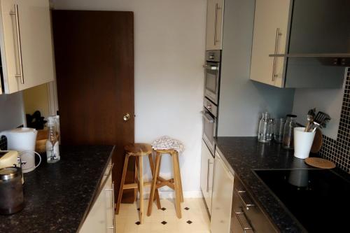 a kitchen with black counter tops and wooden stools at NEW Cosy 2 Bedroom Flat - Englefield Green in Englefield Green