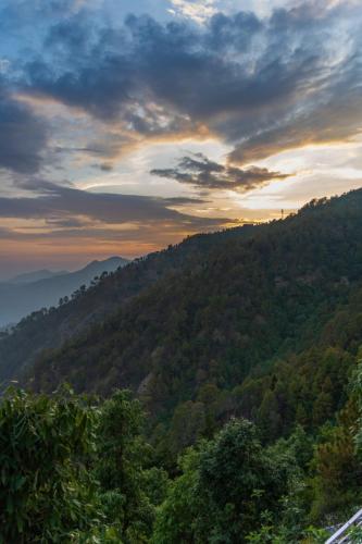 a view of a mountain with a sunset in the background at Ila by Aaryam, Kanatal in Chamba