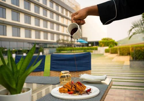 a person pouring sauce into a plate of food on a table at Vivanta Bhubaneswar DN Square in Bhubaneshwar