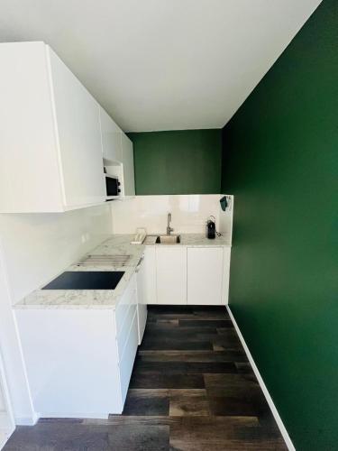 - une cuisine avec des placards blancs et un mur vert dans l'établissement Le Voltaire, Joli Studio, proximité de la Gare et du Centre, Climatisé, à Sète
