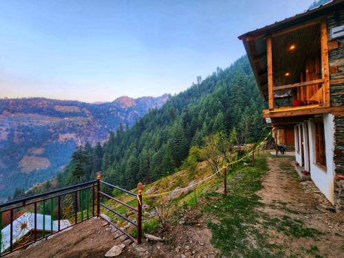 a building on a hill with a view of the mountains at Green Sanctuary Farmstay Sainj in Sainj