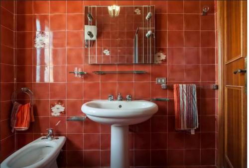 Baño de azulejos rojos con lavabo y espejo en House Via Manzoni, en Terracina