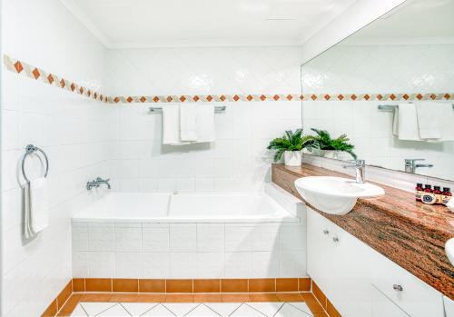 a white bathroom with a tub and a sink at Xanadu Resort in Gold Coast