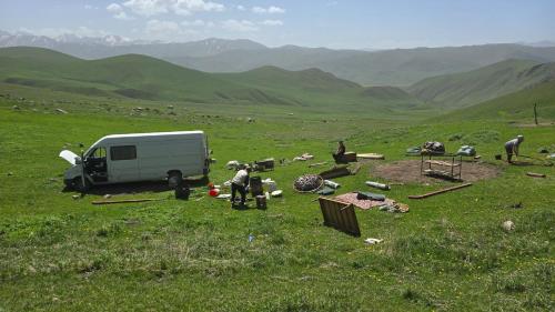 a group of people standing around a van in a field at "Doskulu travel" hostel in Kyzart