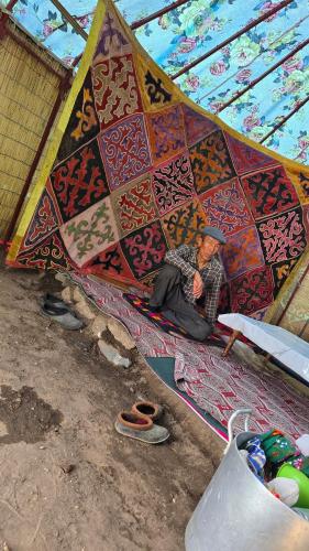 a man sitting on a rug under a large umbrella at "Doskulu travel" hostel in Kyzart