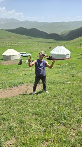a man standing in a field with his hands in the air at "Doskulu travel" hostel in Kyzart