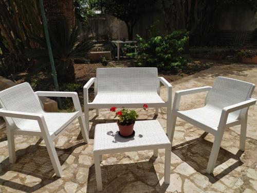 three white chairs and a table with a potted plant at La Rugiada-con giardino privato in Alcamo