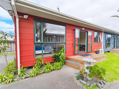 a red house with a porch and a yard at Parakai Geothermal Motel in Parakai