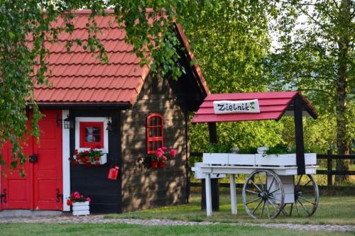 a small house with a red roof and a cart outside at Domki nad jeziorem Widokowo in Reszel