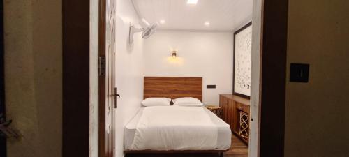 a bedroom with a white bed with a wooden headboard at Birdwing Cottage, Munnar in Munnar