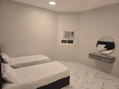 a white room with two beds and a mirror at Malath Furnished Units-ملاذ للوحدات المفروشة 2 in Tabuk