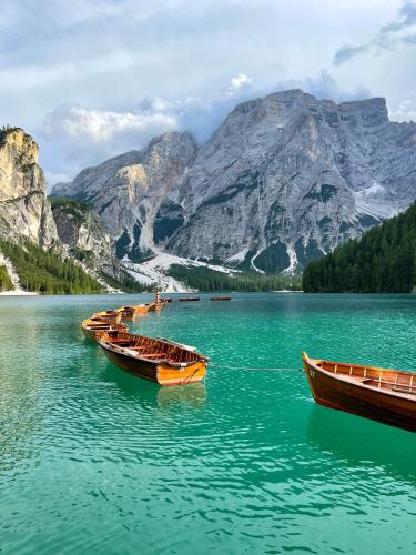 a row of boats on a lake in front of a mountain at The Post Mountain Residence in Dobbiaco