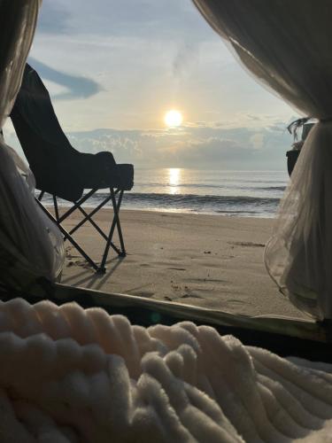 a chair sitting on the beach with the sunset at Earnhomestay sichon in Ban Plai Thon