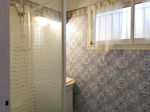 La salle de bains est pourvue de murs carrelés bleus et blancs et d'une fenêtre. dans l'établissement 30m2 - Clim - wifi - 100m des plages, à Fréjus