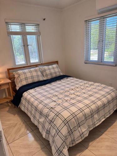a bedroom with a bed with a plaid blanket and two windows at Best Location In Exuma - George Town in Georgetown