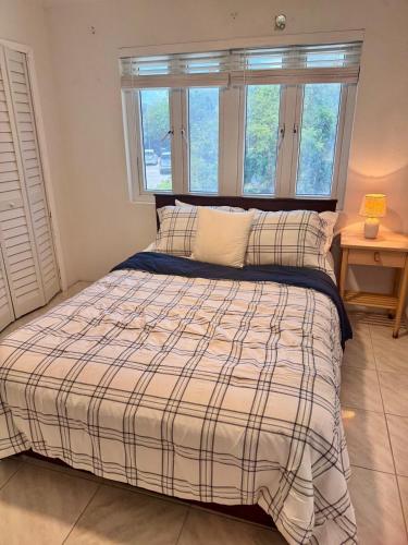 a bedroom with a bed with a plaid blanket and two windows at Best Location In Exuma - George Town in Georgetown