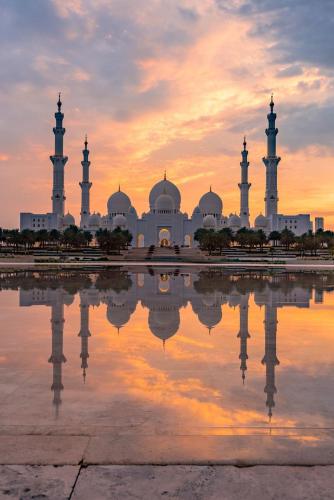 a mosque with its reflection in the water at sunset at Cozy Boho Studio Bright & Airy in Abu Dhabi
