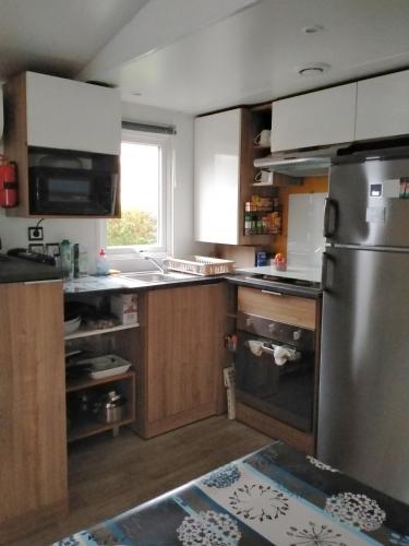 une cuisine avec un réfrigérateur en acier inoxydable et des armoires en bois dans l'établissement Mobil home 3 chambres, à Gastes