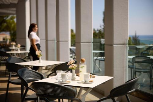 a woman walking on a balcony with tables and chairs at Kiotari Bay in Kiotari