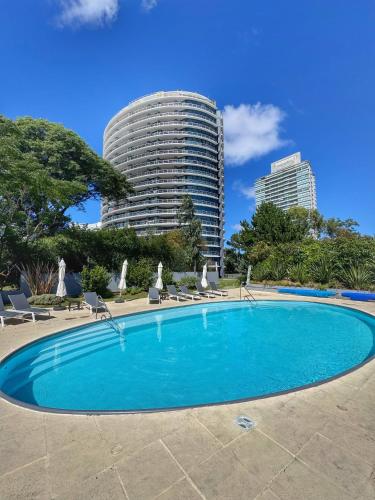 a swimming pool with chairs and a building in the background at Apartamentos Torre Tressesenta in Punta del Este