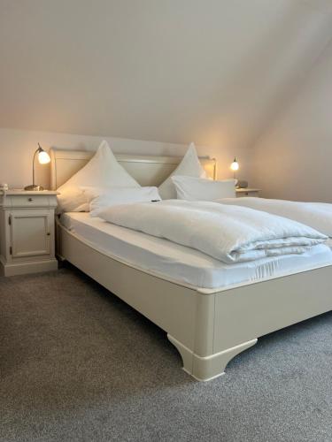 a large white bed with white sheets and pillows at Hotelpension Sanders Höft - Direkt am Strandaufgang in Juist