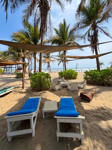 a beach with two lounge chairs and a tent and palm trees at Bambuddha Centro Holistico in Barra Vieja