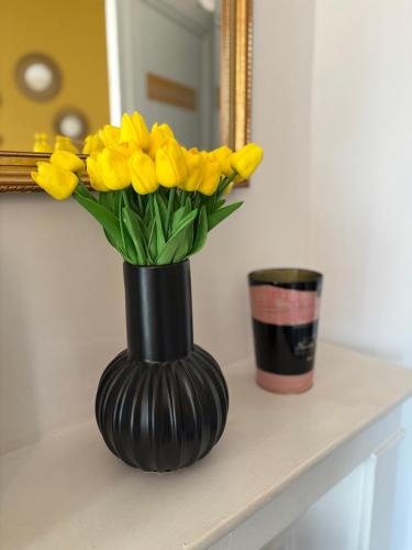 un vase noir rempli de fleurs jaunes sur un comptoir dans l'établissement Pétille en champagne - 1 chambre - Terrasse, à Épernay