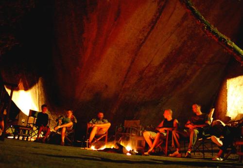 a group of people sitting around a fire on a stage at Big Cave Camp in Matopos
