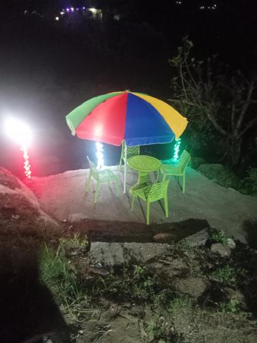 a table and chairs under a colorful umbrella at night at Balkhila bank cafe and camping in Gopeshwar