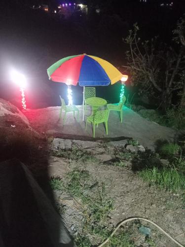 a table and chairs under a colorful umbrella at night at Balkhila bank cafe and camping in Gopeshwar