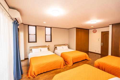 two beds in a room with orange sheets at raikoエレベーター付き大人数向け一棟貸切宿 in Nishi-biwashima