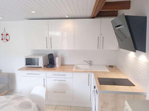 une cuisine avec des armoires blanches, un évier et un micro-ondes dans l'établissement Maisonnette avec Terrasse, Parking à 800m de la Plage - FR-1-778-36, à Dolus-d'Oléron