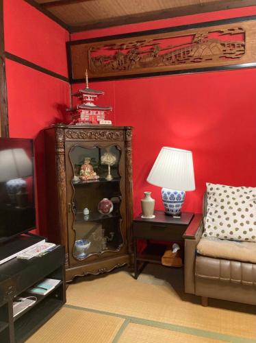 a room with a red wall with a chair and a lamp at ゲストハウス町家はま in Izumi-Sano