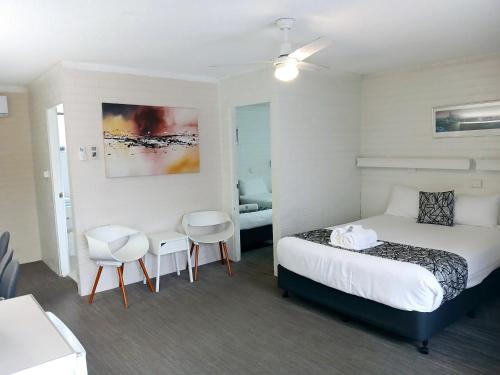 a bedroom with a bed and two chairs in it at Coastal Bay Motel in Coffs Harbour