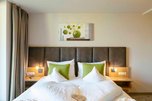 a bedroom with a large bed with white sheets and green pillows at Hotel Pfeiss in Lana