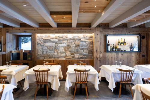 a restaurant with white tables and chairs and a stone wall at Hotel Miralago in Misurina