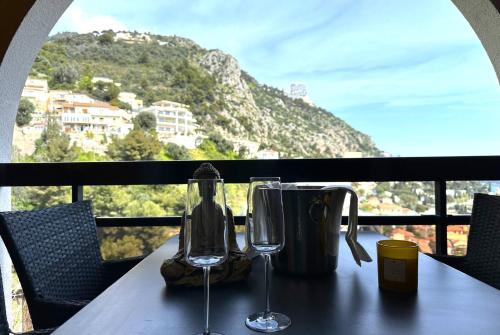 une table avec deux verres à vin assis sur un balcon dans l'établissement STUDIO BEAUSOLEILMONACO TERRASSE VUE MER Clim et Accès Piscine, à Beausoleil