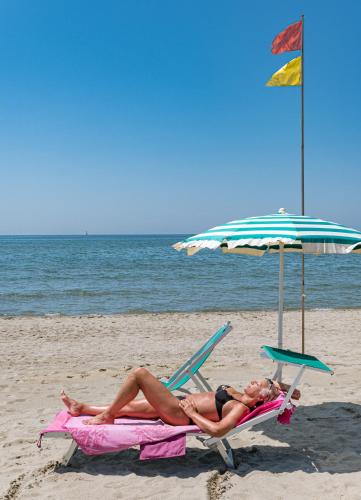 two people laying on the beach under an umbrella at Hotel Tahiti in Viareggio